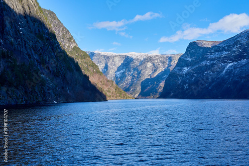Vast Norwegian Fjord Landscape with Majestic Snow-Capped Mountains and Deep Blue Water under Clear Sky with Clouds