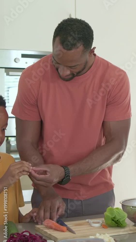 Vertical video: Entering dad salmon tee guiding son, teaching peeling and slicing carrot at island