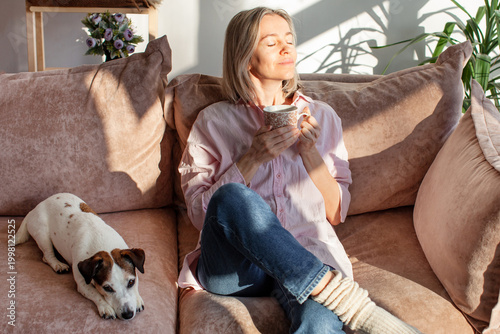 Принти на полотні Positive relaxed smiling attractive woman drinking coffee on couch, meditating daydreaming, enjoying pleasant stress free weekend time alone at home
