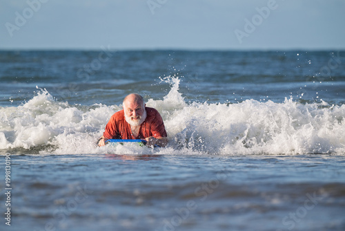 Schilderij op canvas Active senior man boogie boarding toward shore on a sunny summer beach during re