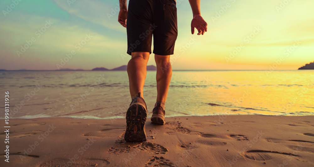 Εκτύπωση καμβά Close-up back view of a fit man walking along the ocean shore at sunset