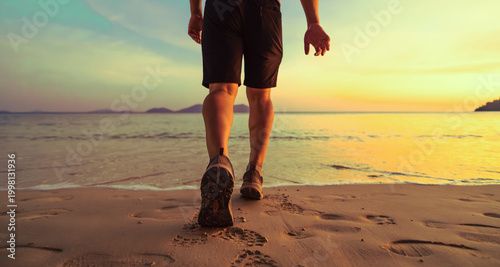 Photography Close-up back view of a fit man walking along the ocean shore at sunset