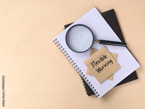 Flexible working text on adhesive note with magnifying glass and notebook. represents modern work-life balance, remote work trends, job searching, and business flexibility