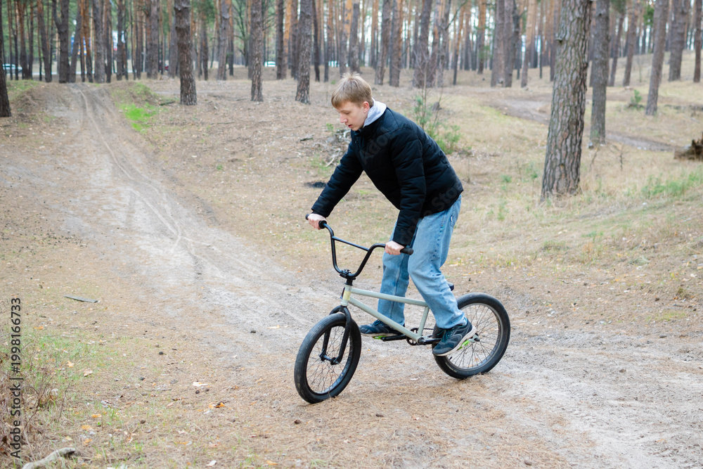 Naklejka premium Teenage Boy Riding BMX Bike on Dirt Path in Pine Forest - Outdoor Extreme Sports and Youth Lifestyle