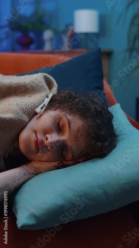 Tired young woman with curly lush hairstyle lying down in bed taking a rest at home room. Carefree girl napping, falling asleep on comfortable sofa with pillows. Closed her eyes enjoy night nap alone
