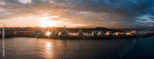 Obraz na plátně Panoramic aerial view of Antibes, France, shows superyachts at Port Vauban as the sun sets behind low mountains, old town bastions on the right, calm harbor water glinting