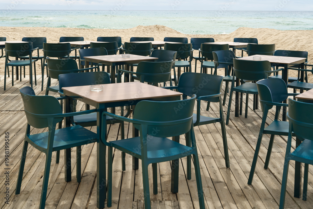 Behang Empty beach cafe terrace with neatly arranged tables and chairs facing the sea