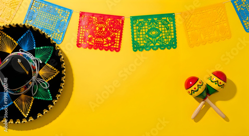 Mexican fiesta celebration background with sombrero, maracas and papel picado banners, traditional cinco de mayo party decorations on yellow surface