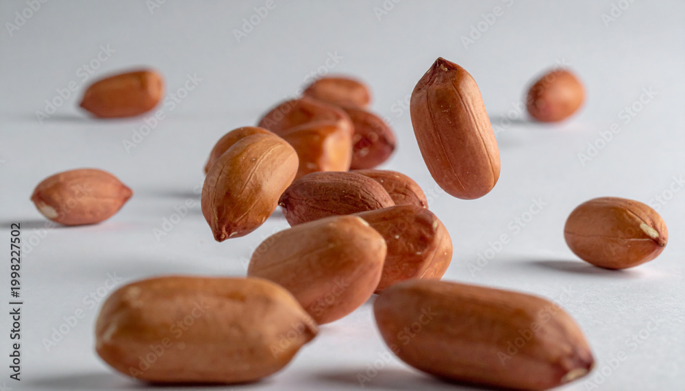 Obraz premium Close-up of shelled peanuts in motion against a neutral gray backdrop