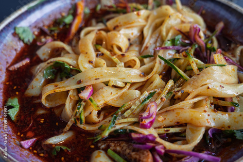 Close-up of Chinese Liangpi cold skin noodles in spicy chili oil with fresh vegetables