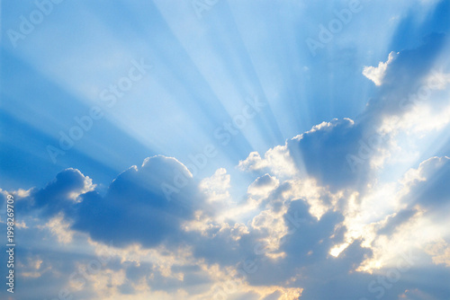 Dramatic sky with sun rays shining through fluffy white clouds