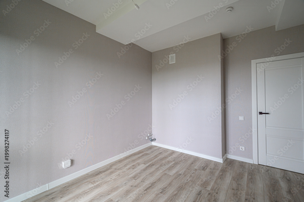 Obraz premium clean, empty room with light grey walls, wooden laminate flooring, white ceiling, one white interior door, minimal fixtures, neutral tones, ready for furnishing