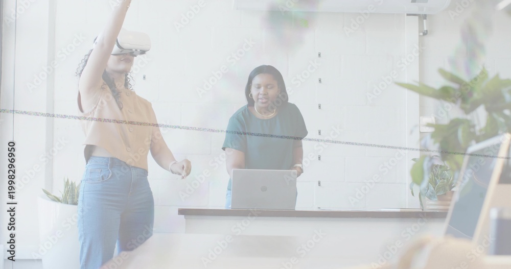 Obraz premium Interacting two women wearing VR headset and tee, testing on laptop at long conference table