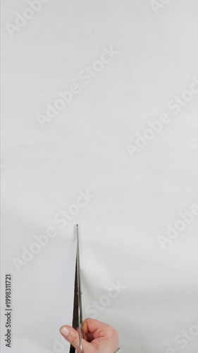 Close-up of a hand in a sweater cutting white paper with scissors on a wooden table