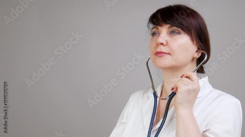 Female healthcare professional with brown hair adjusts stethoscope around neck, listens intently, and prepares to check patients heartbeat in a clinical setting