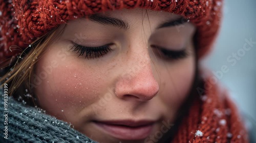 Footage close-up of a young woman with closed eyes wearing a red knitted hat and scarf as snowflakes fall, calm winter mood, shallow depth of field outdoors