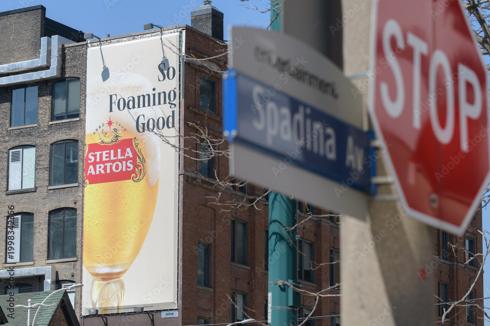 Fototapeta premium wall mounted advertising banner on the exterior brick building for Stella Artois, a beer, incl defocused traffic signs, Toronto Spadina Av