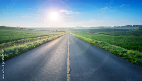 An endless road stretches across green fields under a blue sky with soft sunlight.