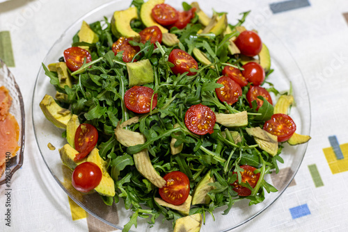Salad with arugula, avocado, cherry tomatoes in a transparent glass plate.