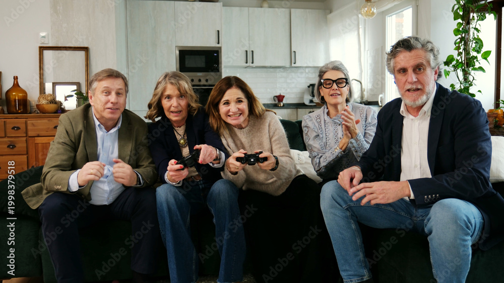 Fototapeta premium Senior people sitting on a sofa playing video games and having fun