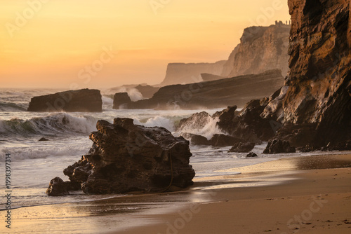 Natural sea arch at Hole in the Wall Beach in California during sunset, warm golden light illuminating rugged coastal rock, ocean waves and smooth sand, creating dramatic seaside landscape