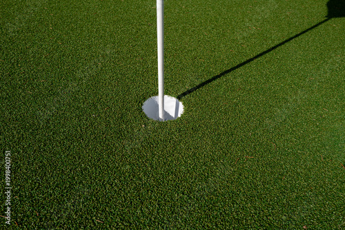 Close-up detail of a golf hole with flagstick on an artificial turf putting green.