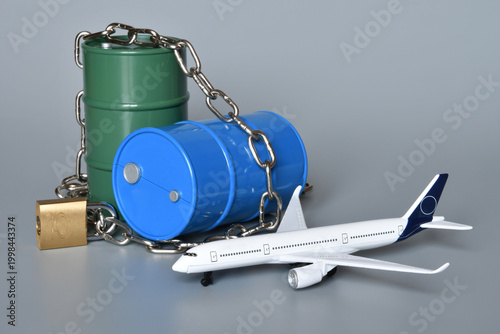 Miniature oil barrels locked with a chain and padlock, along with an airplane. Concept of the shortage and rising price of jet fuel due to the Middle East crisis and the war in Iran.