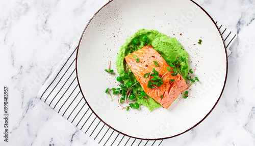 Grilled salmon filet served on a bed of green pea puree with fresh microgreens and peas, presented on a white plate
