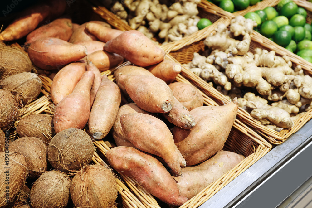Fototapeta premium Sweet potatoes in baskets. Fresh market produce background. Ginger coconuts limes detail. Organic grocery display. Healthy tropical ingredients. Natural food selection.