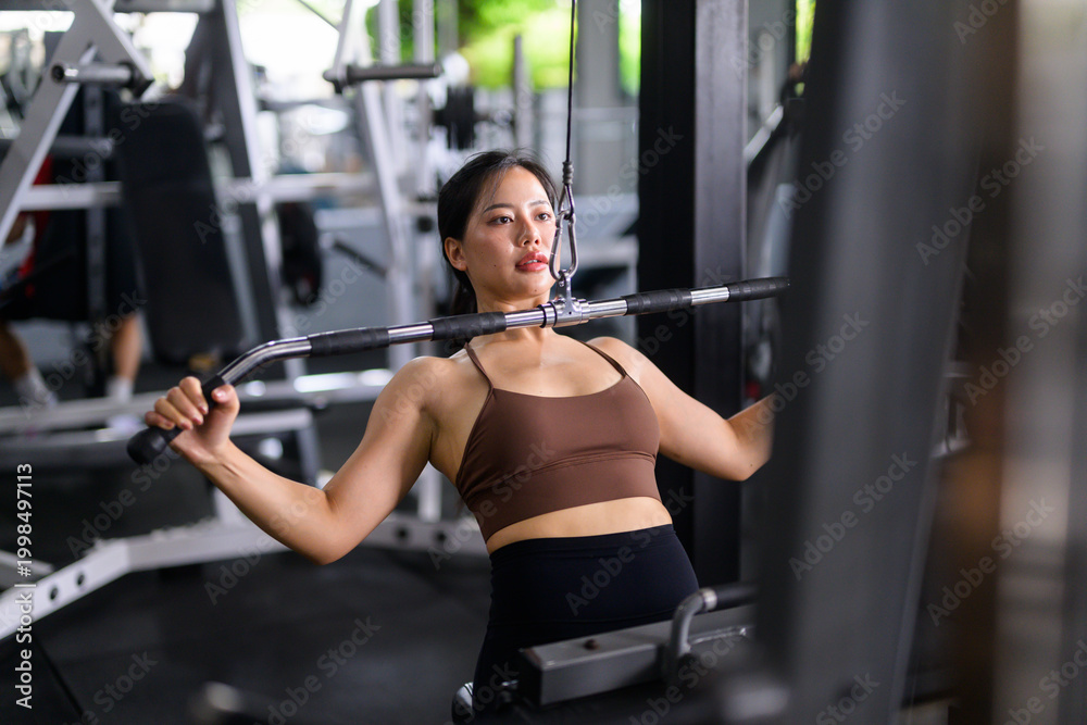 Fototapeta premium Young Asian woman training back muscles at a modern gym
