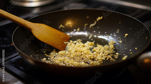 Close up view of finely chopped garlic and ginger saute in hot oil in a dark pan with a wooden spatula, a culinary process for delicious meals