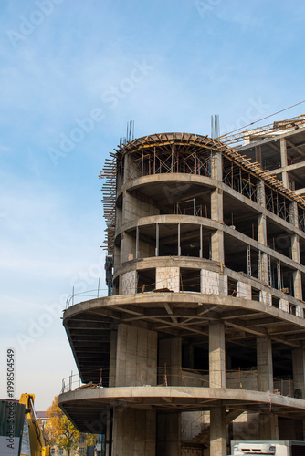 Photos A construction tower crane operates against the backdrop of an unfinished building and a blue sky