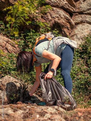 Fotografie Mature female volunteer cleaning up garbage and plastic waste in a forest