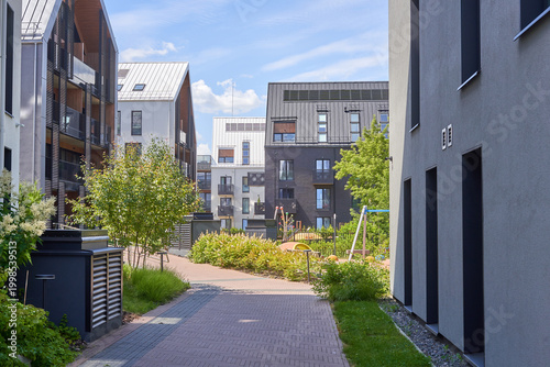 Modern residential apartment complex featuring contemporary Scandinavian-influenced architecture with mixed materials including wood paneling, metal roofing, and concrete facades. The scene shows a