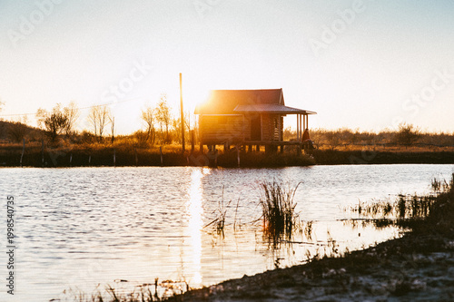 Fotografi Lakeside house at sunset with calm water reflections