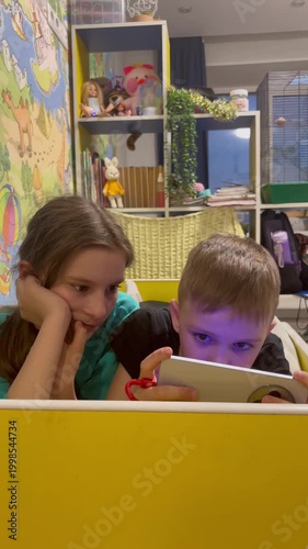 Two children boy and girl, play games or watch informational video text on Internet on mobile phones and tablet computers at home on sofa. Leisure, children, digital technology and people concept