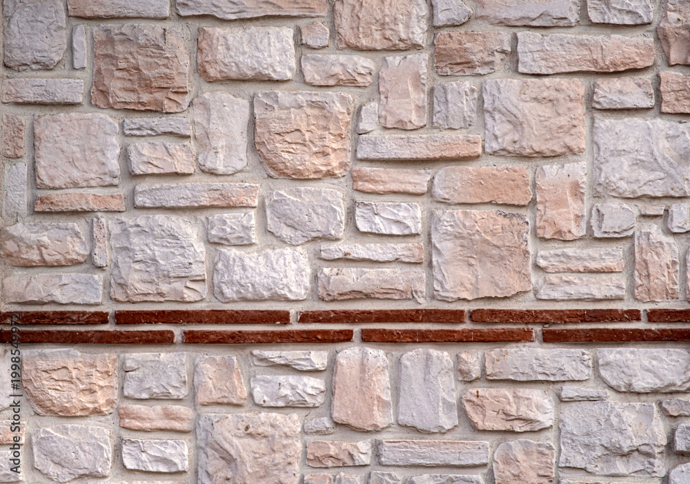Fototapeta premium Stone wall texture with mixed natural rocks and brick detail. Rustic masonry background with neutral tones for architectural and design use. Rich texture, varied sizes.