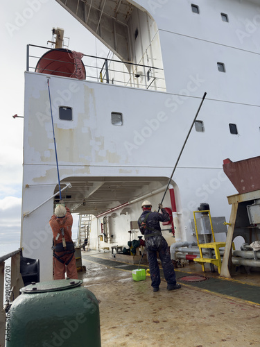 Fotografie deck crew of the cargo ship painting superstructure by rollers