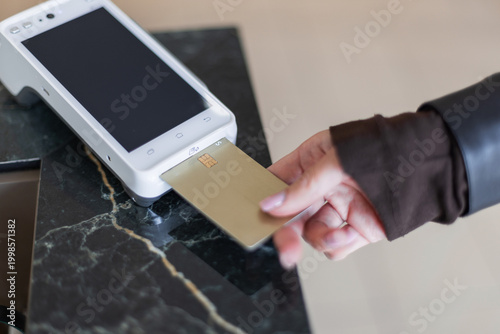 Fotografie Close-up of a hand inserting a gold credit card into a white terminal for a chip-and-pin transaction