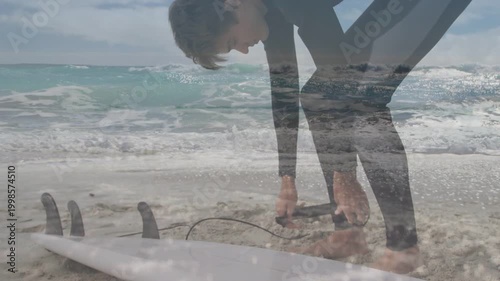 Male surfer bending and fastening ankle leash by surfboard, grabbing cord, preparing for surfing