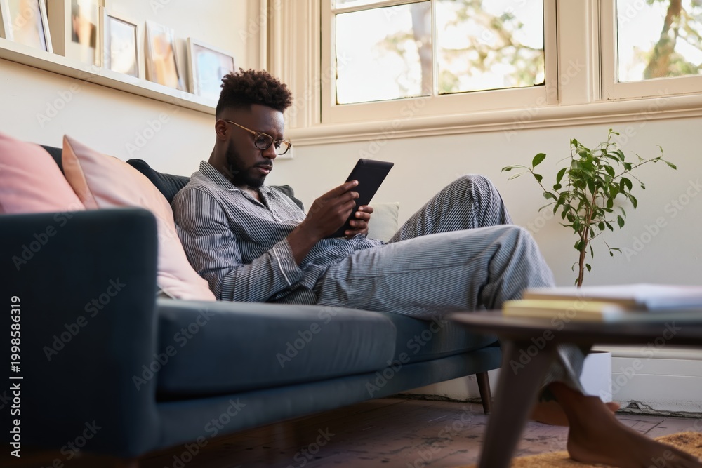 Fototapeta premium Man using tablet reclining on sofa in living room during daytime