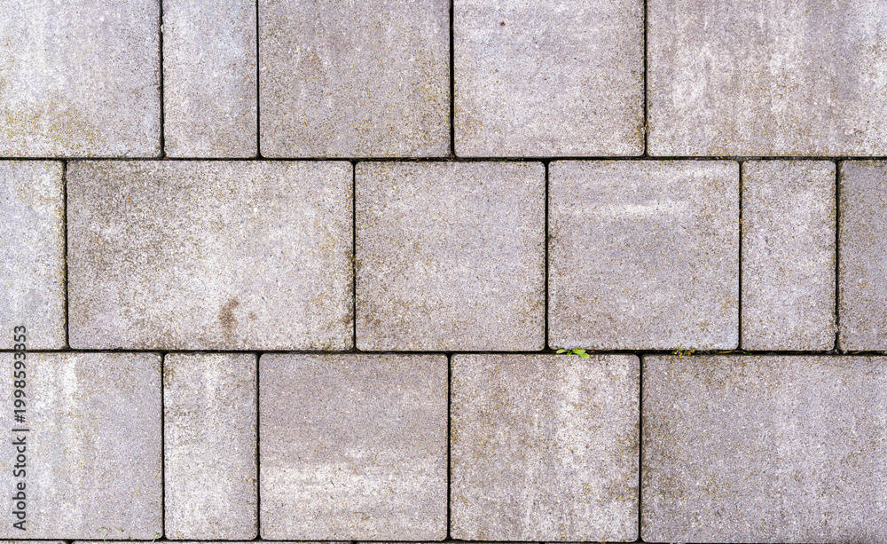 Fototapeta premium A close-up view of a textured concrete pavement featuring a regular pattern of rectangular stones. The image showcases wear and minor imperfections, suitable for architectural and landscaping project