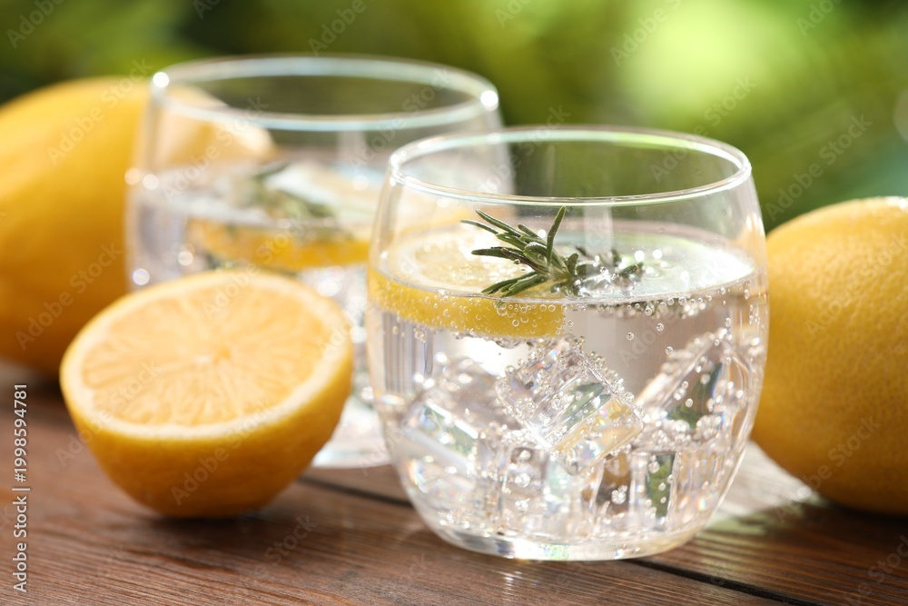 Fototapeta premium Sparkling water with lemon and rosemary on wooden table against blurred background, closeup