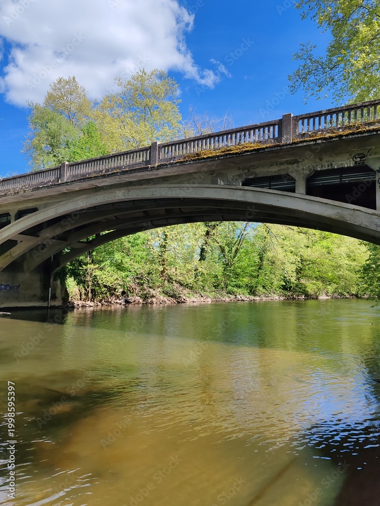 Obraz premium Stone bridge crossing calm river under blue spring sky