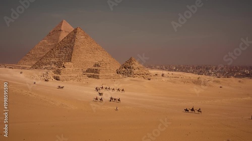 Tourists walking and riding camels in desert valley with Giza pyramids. A cinematic view of desert valley near Giza plateau, with tourists exploring on foot, riding camels, and in horse-drawn carriage