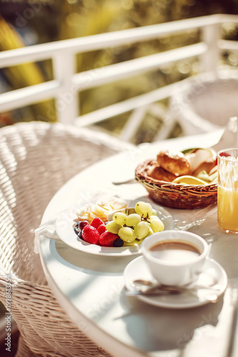 breakfast on terrace with coffee fruits and pastries, sunlight, cozy atmosphere, outdoor relaxation, summer morning