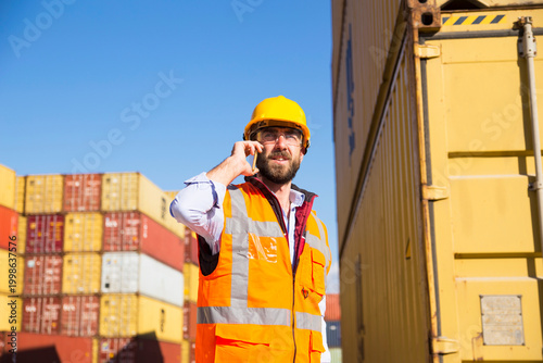 Construction worker in hard hat and safety vest operates radio at shipping container yard