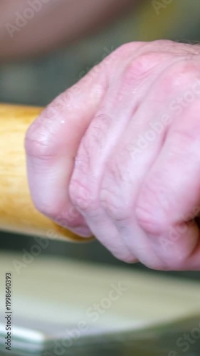 Woman baker is rolling out dough using wooden rolling pin on cozy wooden table. She is rolling dough in flour, preparing it for an Italian pizza with tomato and cheese.