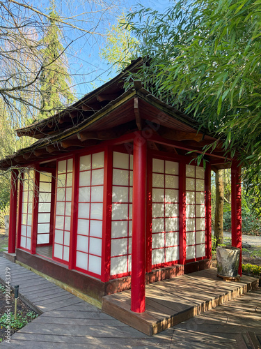 Japanese garden pavilion with red columns and sliding paper panels surrounded by bamboo and trees
