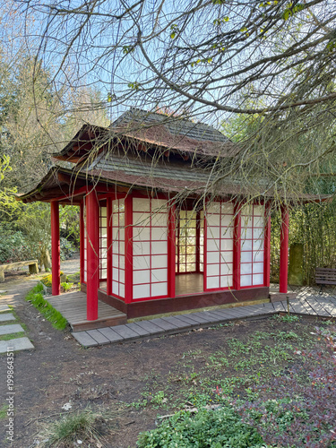 Japanese garden pavilion with red columns and sliding paper panels surrounded by bamboo and trees